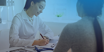 Image shows a female doctor writing with a female patient in front of her